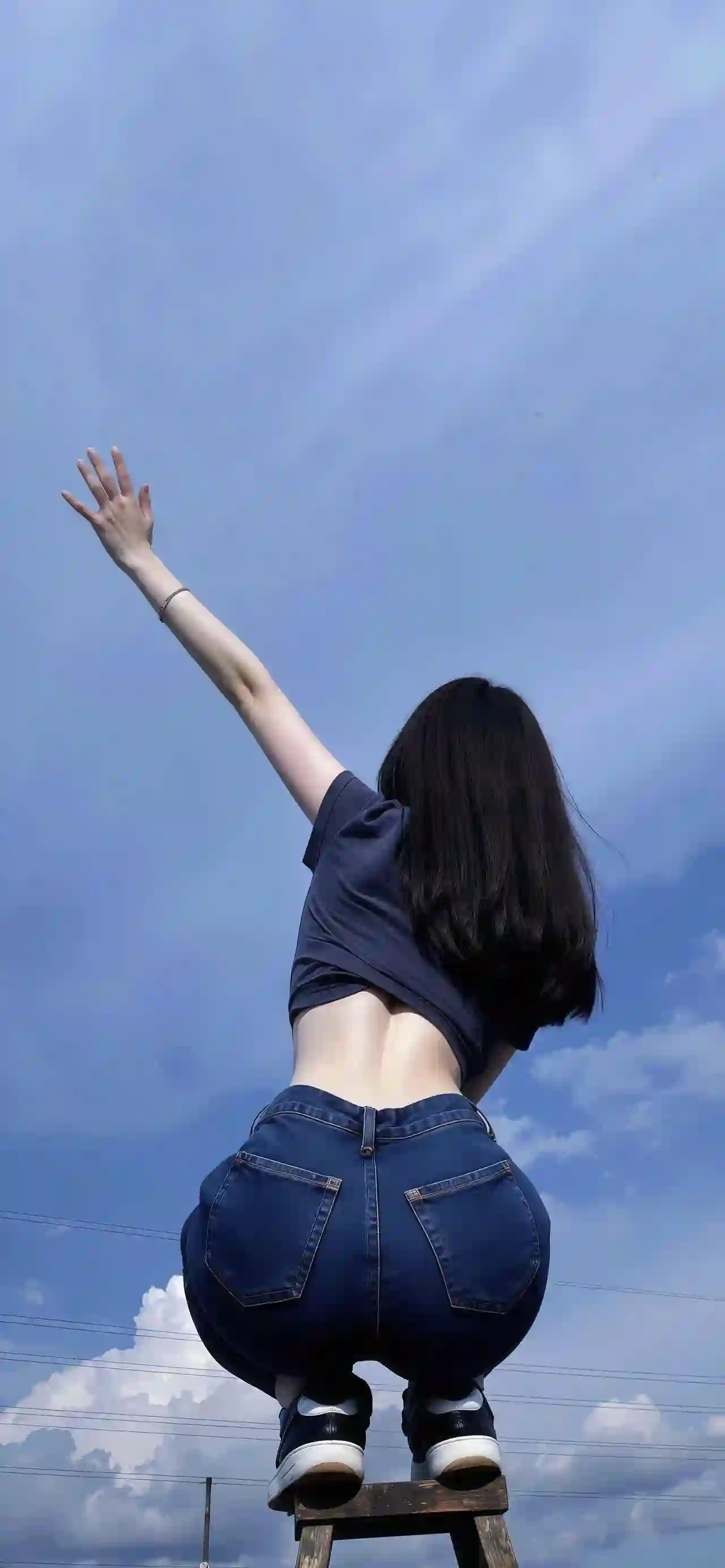 长发女孩站在梯子上 背对镜头 右手高举伸向广阔的蓝天 画面以仰拍视角突显人物舒展的姿态与清新的氛围 背景为晴朗的天空与云彩