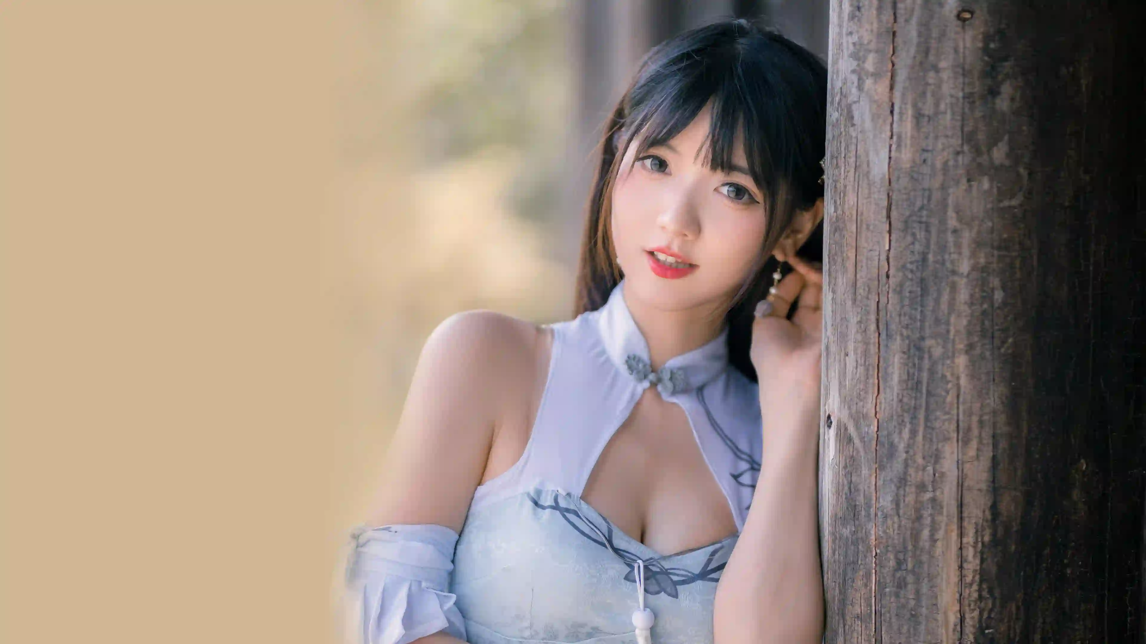 一位黑发长发美女身穿浅蓝色旗袍，倚靠在木柱上，面带微笑，背景模糊，光线柔和，营造出唯美古风氛围。