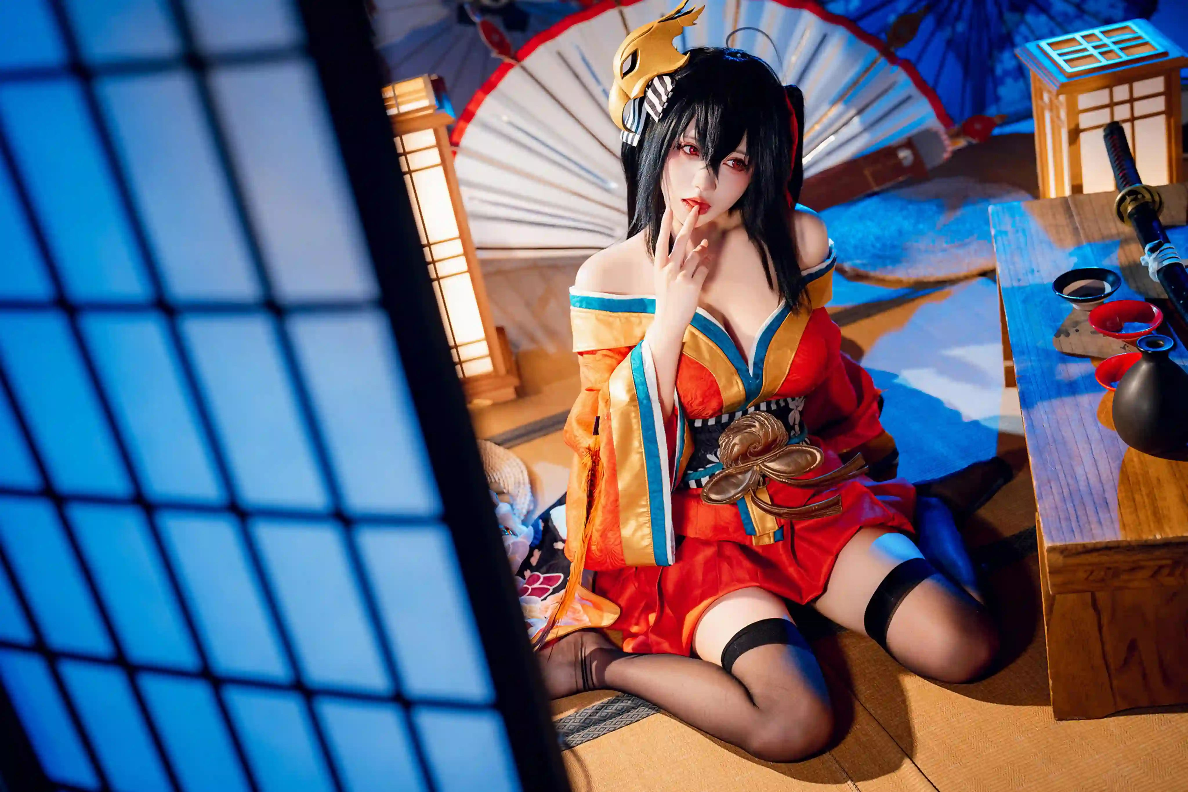 一位黑发红眼的少女cosplay成游戏或动漫角色，穿着红金色和服，跪坐在日式室内场景中，背景有日式窗户、灯笼、扇子和武器等元素，营造出唯美氛围。