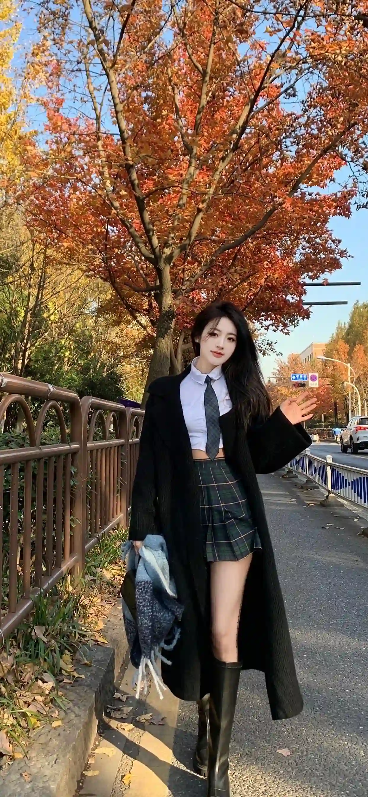一位长发少女在秋天的街道上 穿着格子短裙 白色衬衫 领带和黑色长外套 手持围巾 背景是红叶树木 展现优雅时尚的秋季氛围