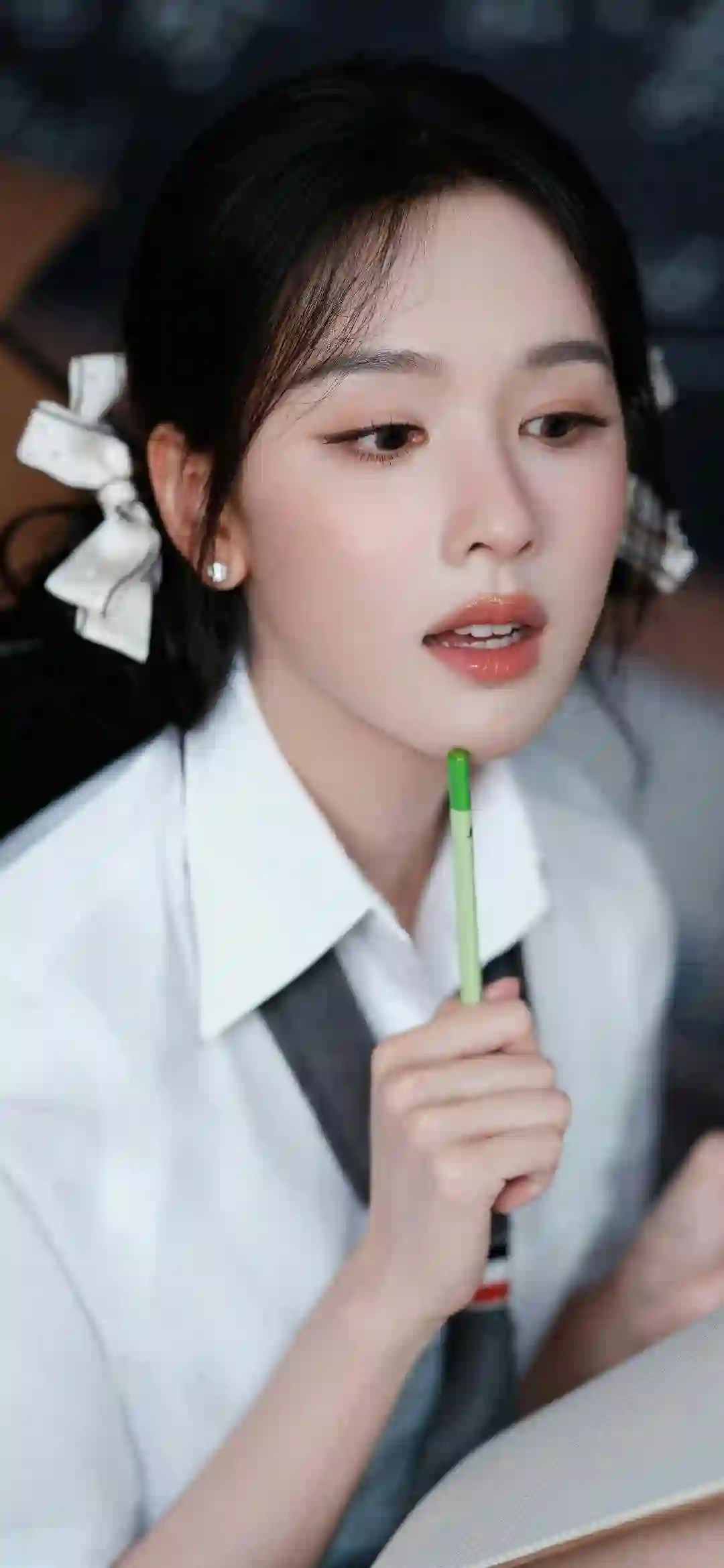 一位穿着白衬衫系领带的少女 手持绿色铅笔 头发上有白色蝴蝶结发饰 表情专注