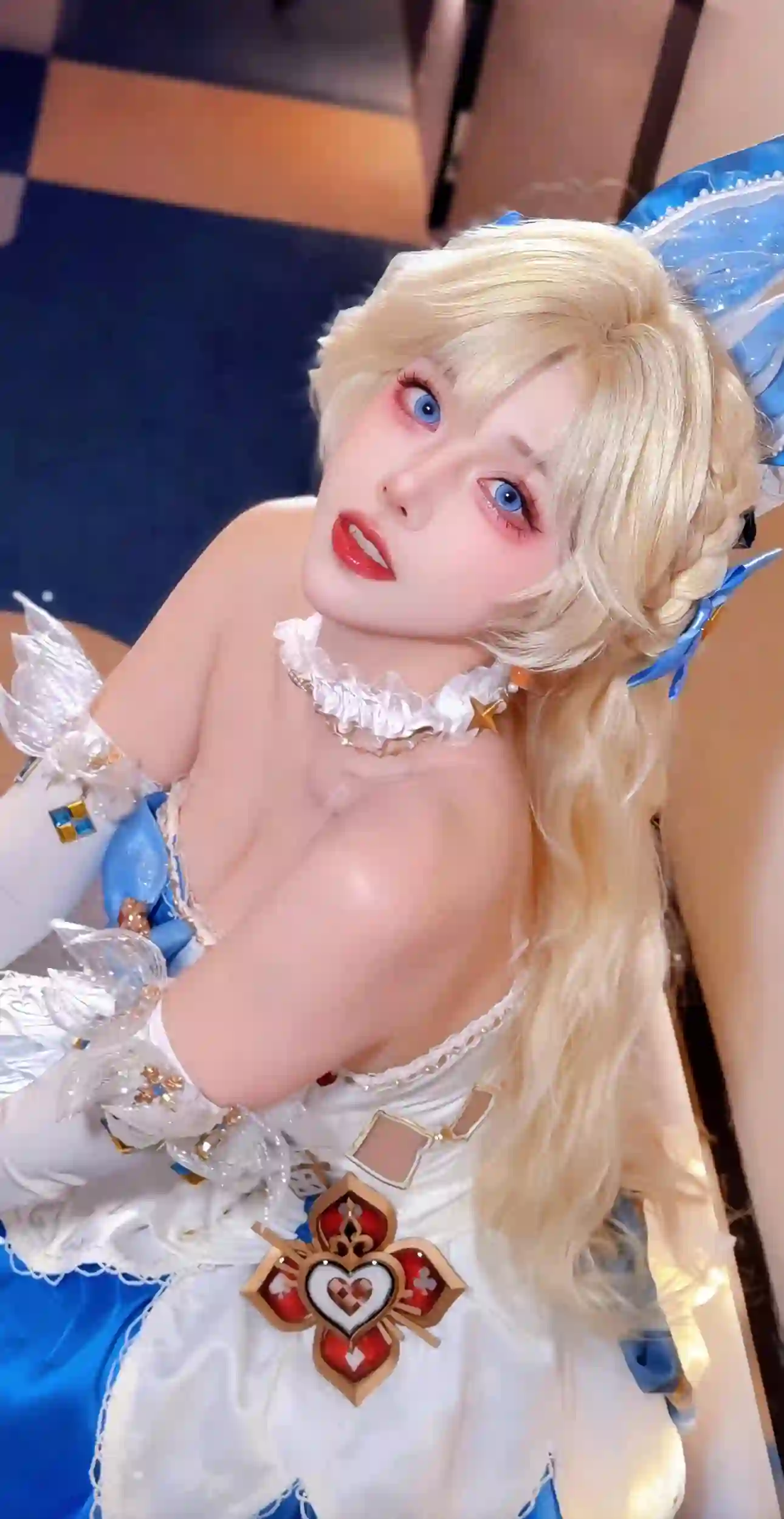 一位女性cosplayer穿着白色和蓝色相间的服装，金色长发，蓝色眼睛，服装上有扑克牌花色（红桃、梅花、方块）装饰，整体造型精致可爱。
