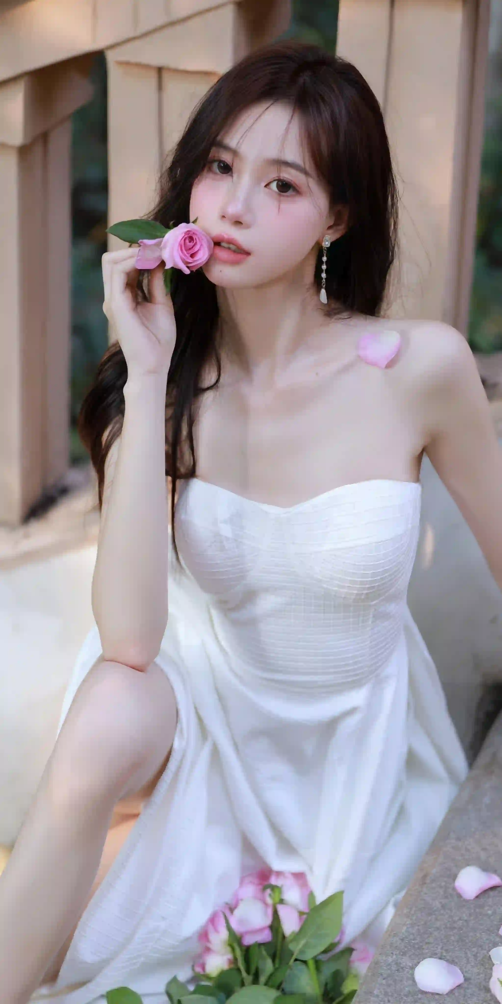 一位穿着白色抹胸连衣裙的年轻女性 手持粉色玫瑰 坐在户外栏杆旁 妆容精致 氛围优雅唯美