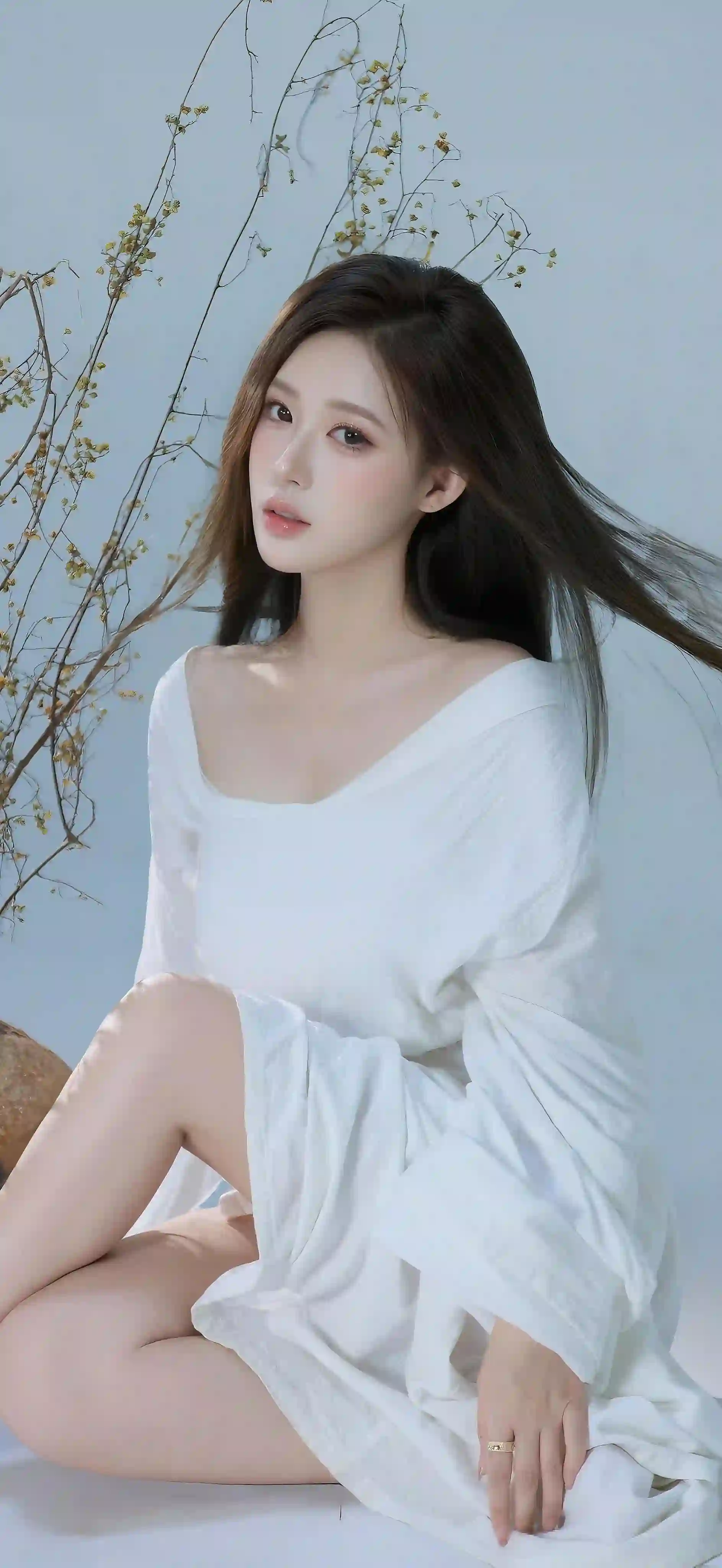 一位穿着白色长裙的年轻女性坐在浅蓝色背景前 长发飘逸 干枝植物装饰 整体氛围清新优雅