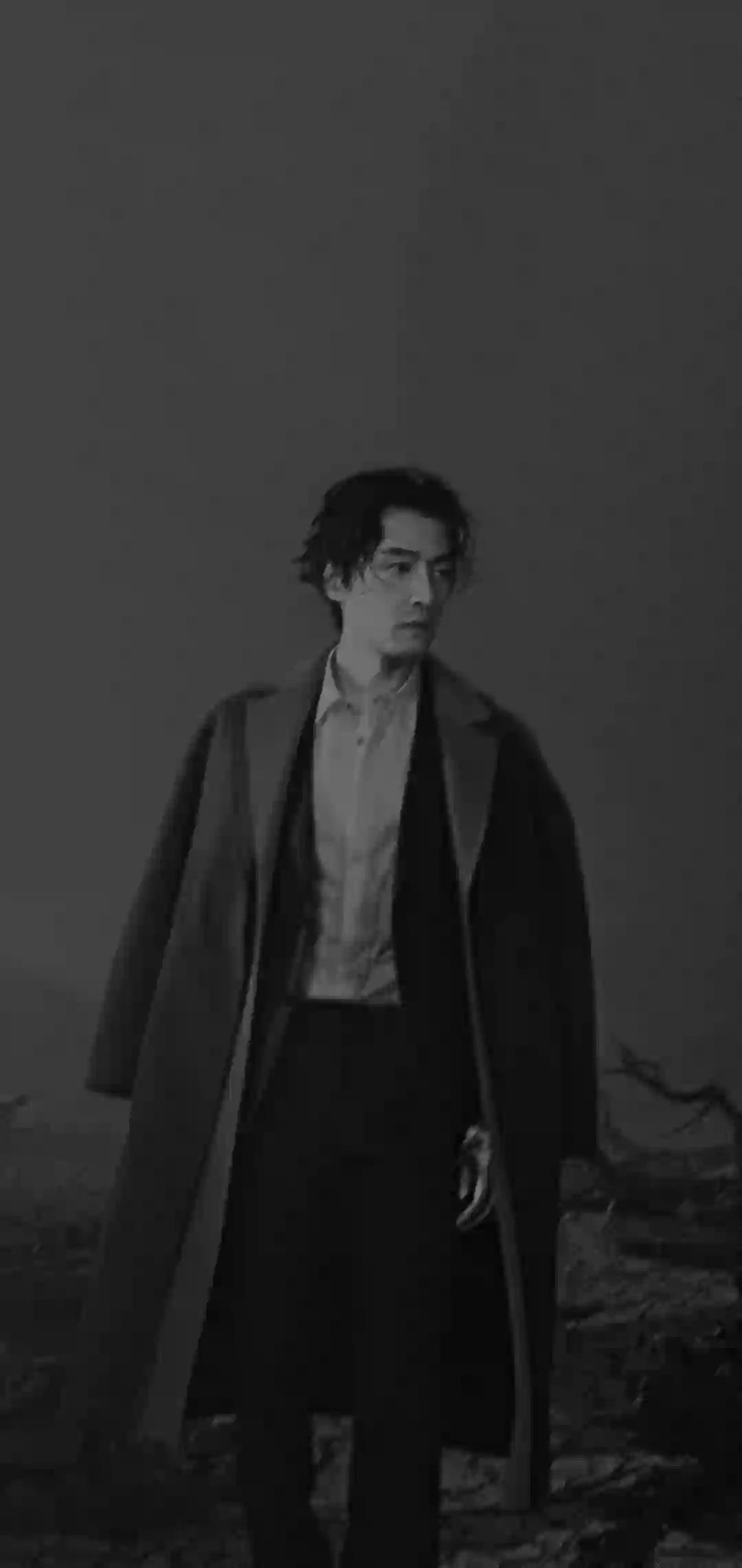 图片展示了一位穿着长风衣和白色衬衫的男性 站在荒野环境中 采用黑白摄影风格 氛围暗淡而神秘
