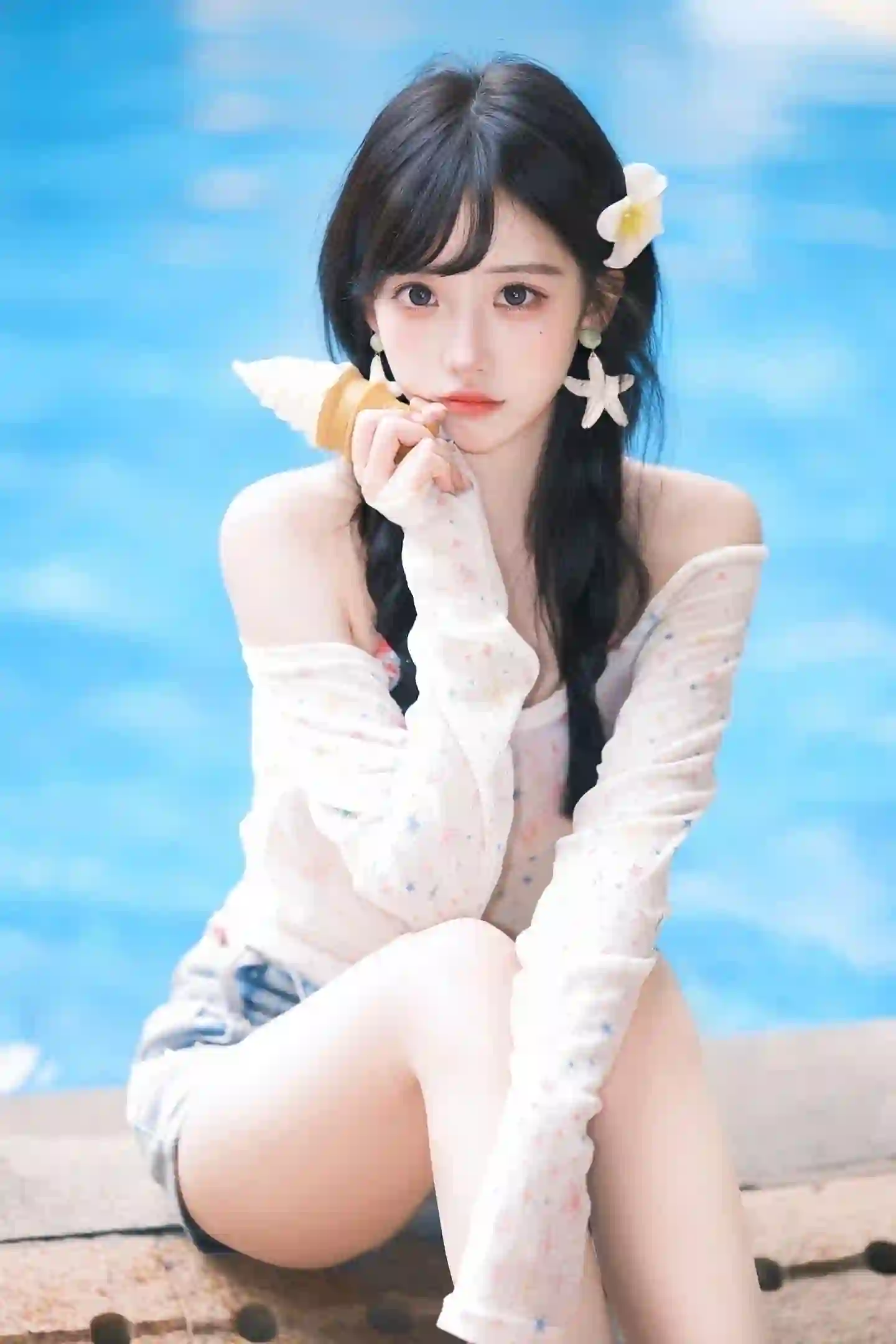 一位黑色长发女孩坐在泳池边，头戴白色鸡蛋花发饰，佩戴星星耳环，身穿白色露肩星星图案上衣和牛仔短裤，手持冰淇淋甜筒，背景为蓝色泳池水面，整体风格清新甜美
