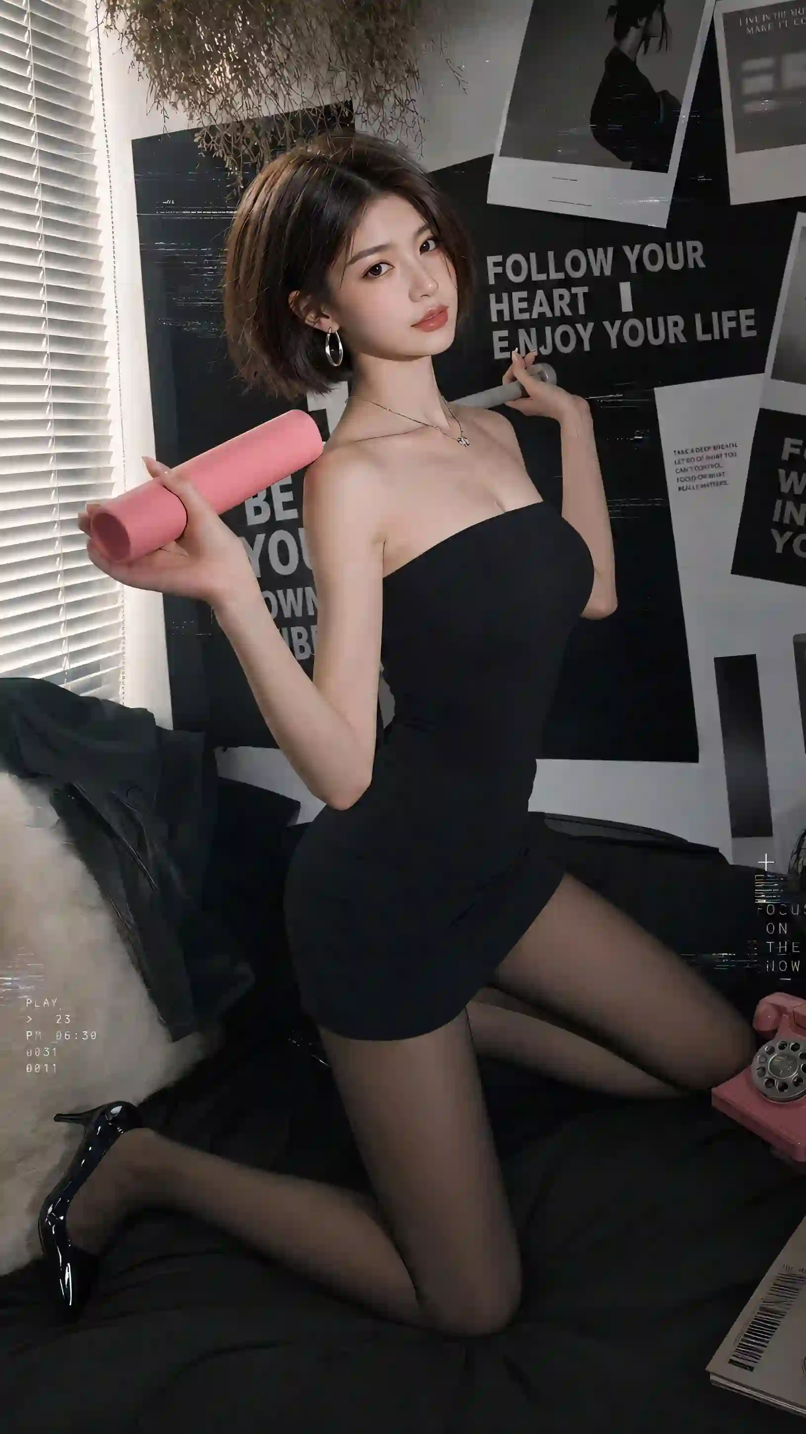 一位短发美女穿着黑色抹胸裙和黑丝，跪坐在床上，手持粉色物品，背景有时尚海报和百叶窗。